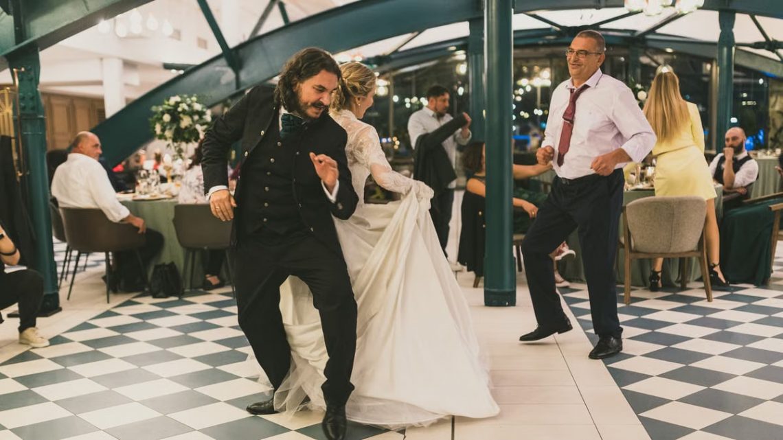 Lively wedding dance with bride, groom, and guests in elegant indoor setting.