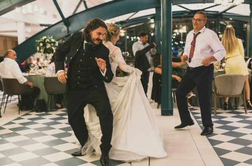 Lively wedding dance with bride, groom, and guests in elegant indoor setting.