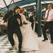 Lively wedding dance with bride, groom, and guests in elegant indoor setting.