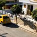 Cozy urban street scene featuring a parked yellow car under bright sunlight, beside modern houses.